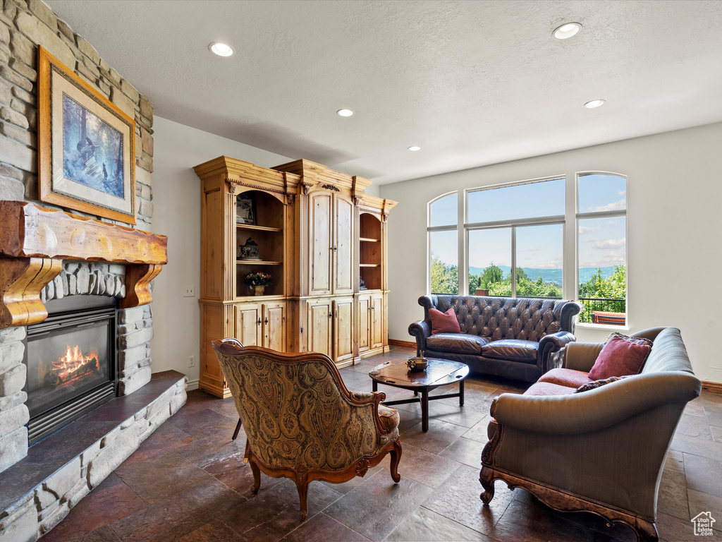 Living area featuring stone tile floors, recessed lighting, a stone fireplace, baseboards, and a textured ceiling