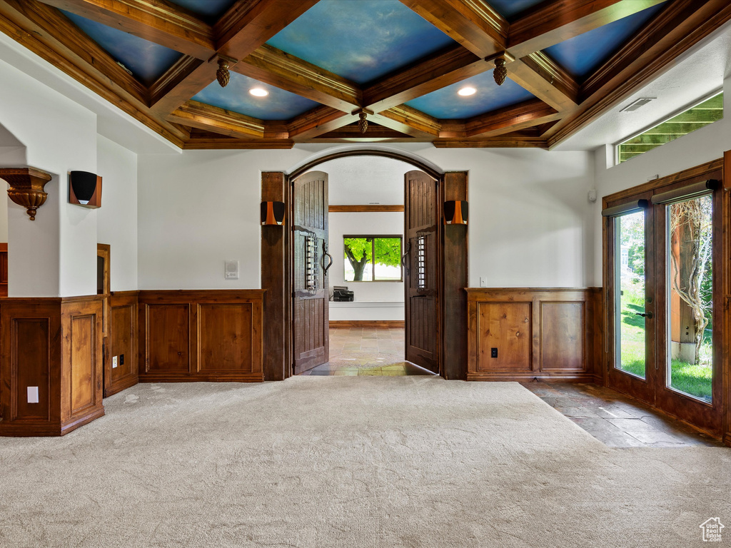 Unfurnished room with carpet, a wainscoted wall, beam ceiling, coffered ceiling, and arched walkways