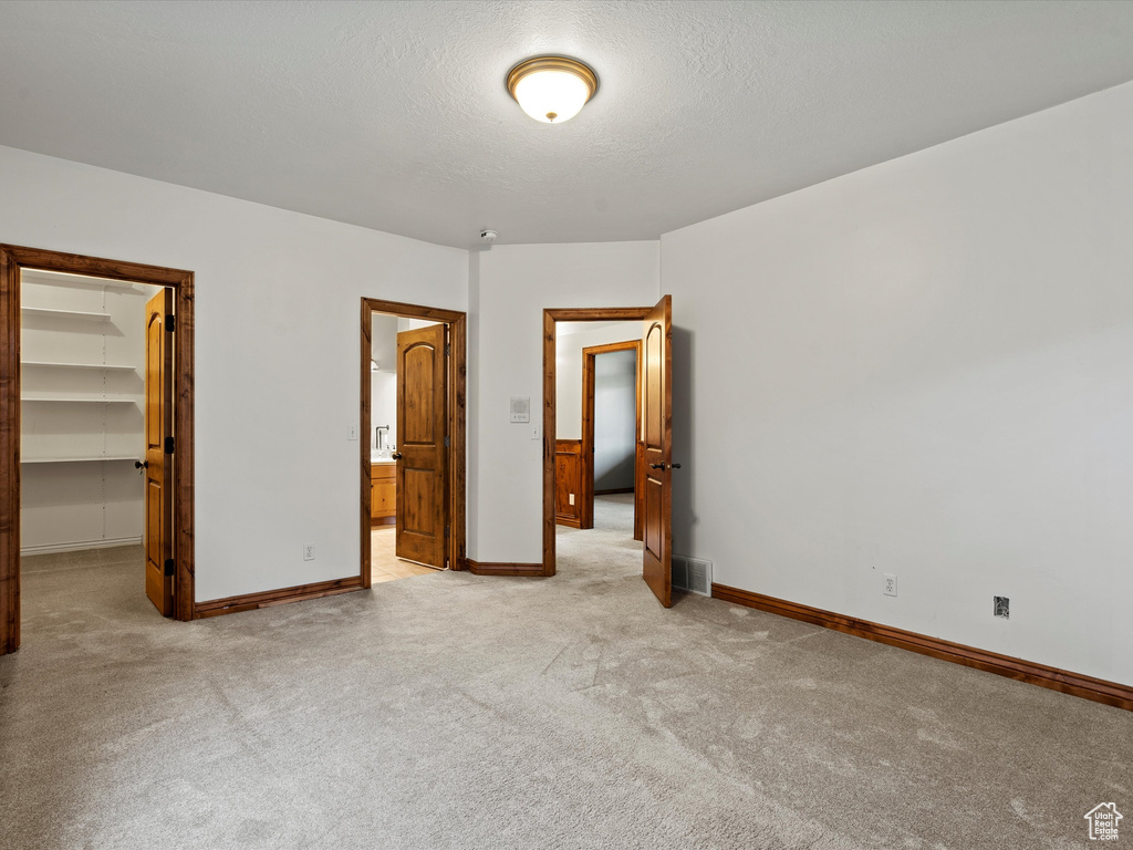 Unfurnished bedroom with a walk in closet, light colored carpet, baseboards, a closet, and a textured ceiling