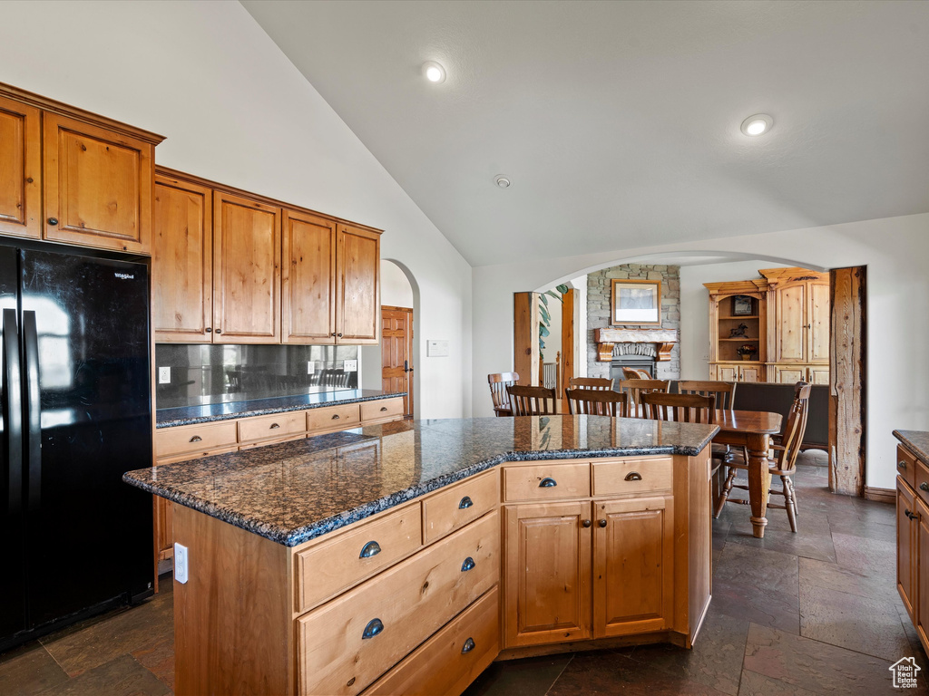 Kitchen featuring freestanding refrigerator, arched walkways, decorative backsplash, a center island, and high vaulted ceiling
