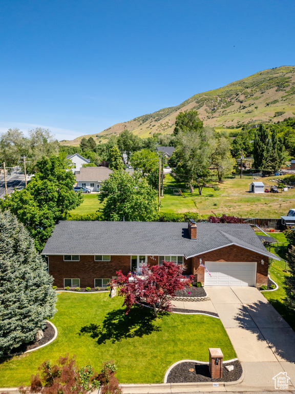 View of front of house with a mountain view, concrete driveway, brick siding, a front lawn, and an attached garage