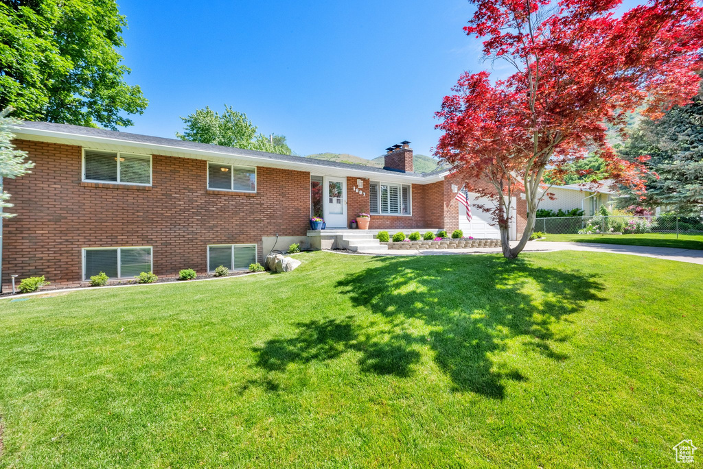 Ranch-style home with an attached garage, brick siding, a chimney, a front yard, and driveway