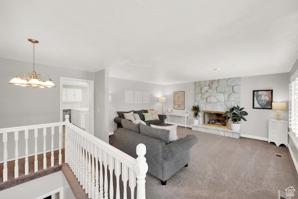 Carpeted living area with baseboards, a stone fireplace, and a chandelier