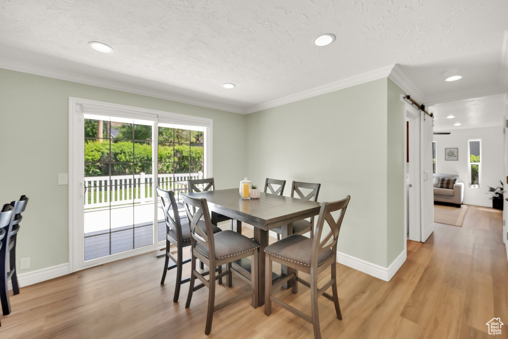 Dining space featuring a barn door, light wood-type flooring, ornamental molding, recessed lighting, and baseboards