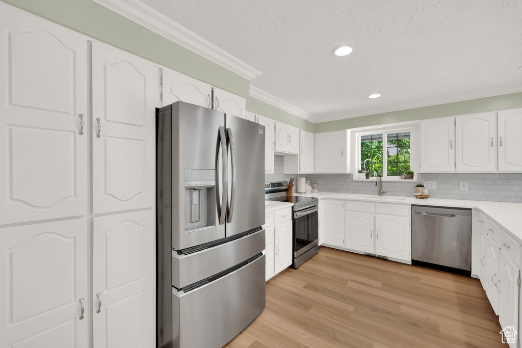 Kitchen featuring appliances with stainless steel finishes, a sink, ornamental molding, a textured ceiling, and white cabinetry