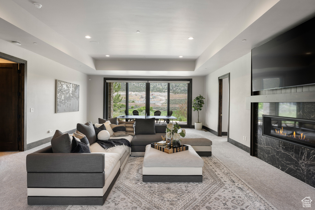 Living area with carpet flooring, baseboards, a raised ceiling, a premium fireplace, and recessed lighting