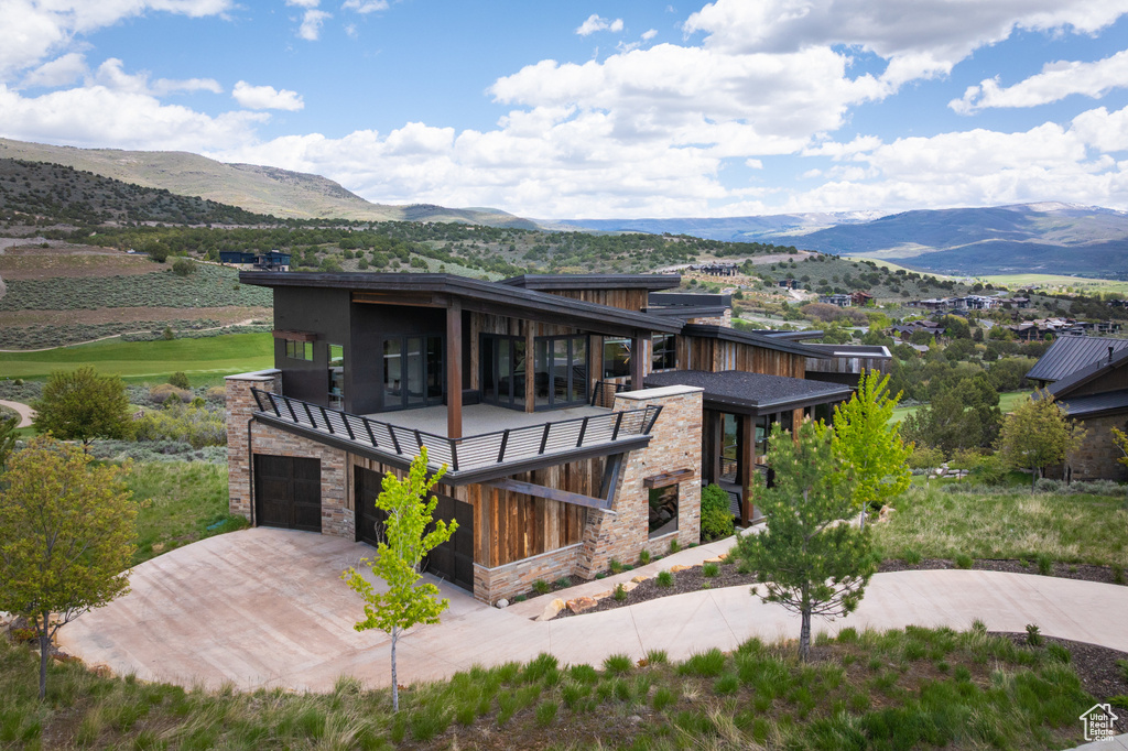View of front facade featuring a mountain view, a balcony, stone siding, and driveway