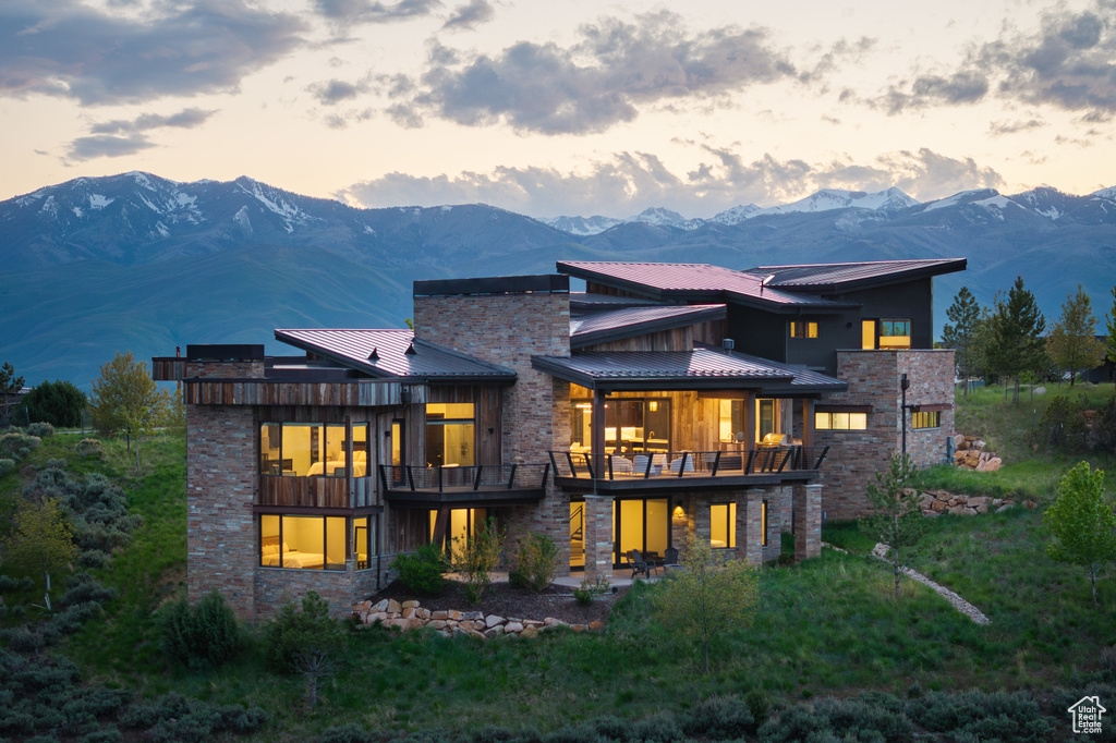 Back of house at dusk with a mountain view, stone siding, metal roof, and a standing seam roof