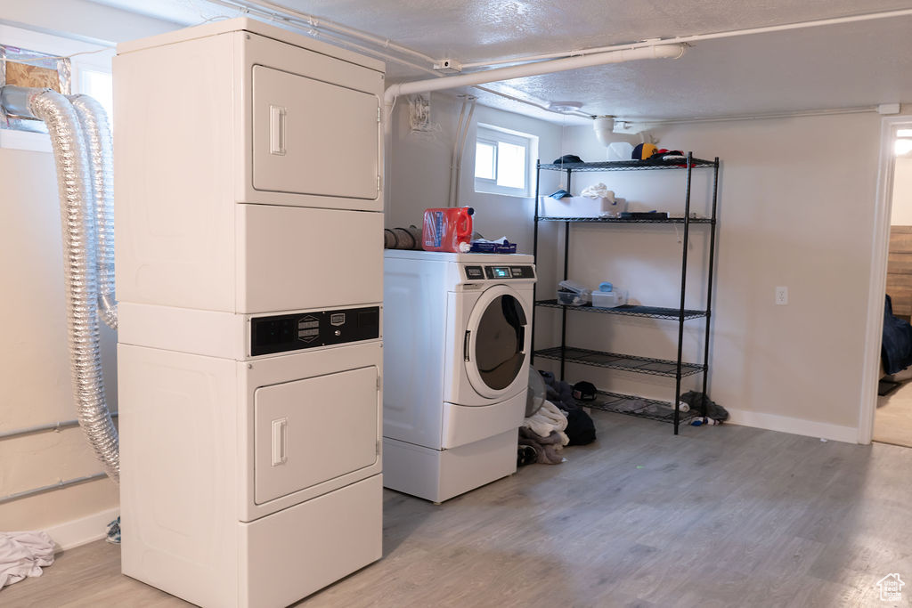 Laundry area featuring stacked washer and clothes dryer, light wood finished floors, and baseboards