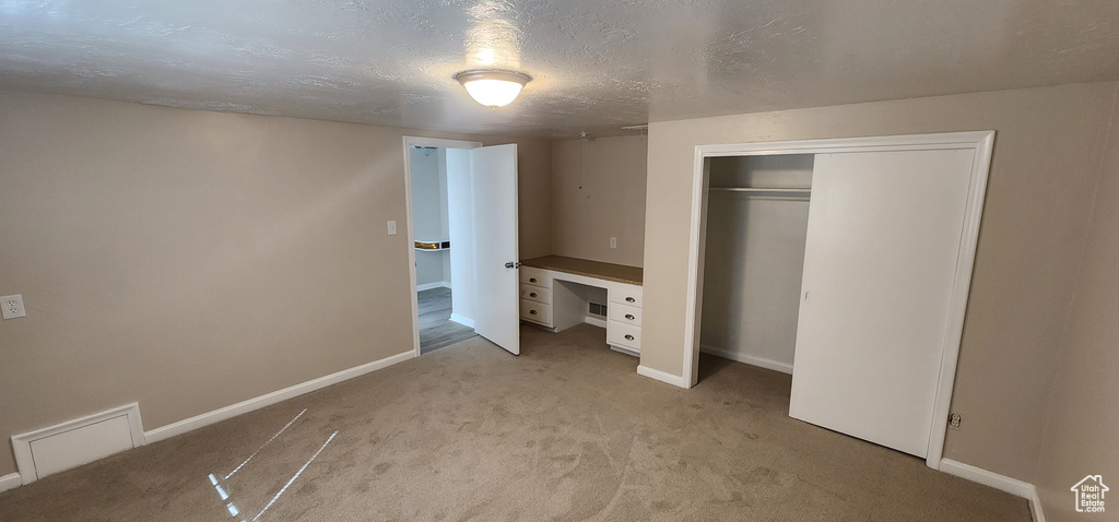 Unfurnished bedroom featuring baseboards, light colored carpet, a closet, and a textured ceiling