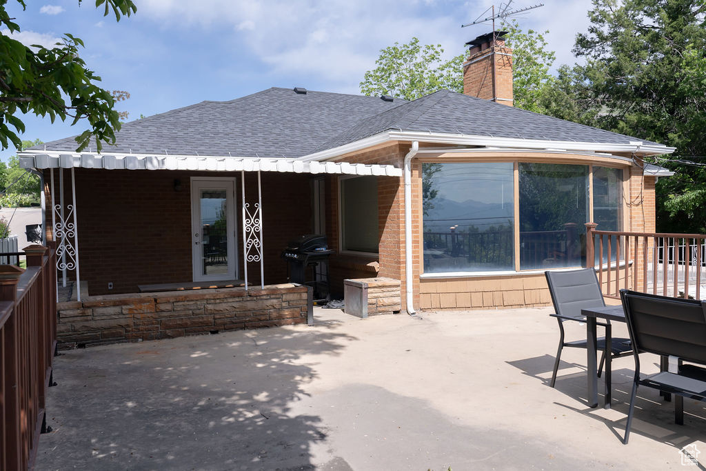 Rear view of property with roof with shingles, brick siding, a patio area, and a chimney