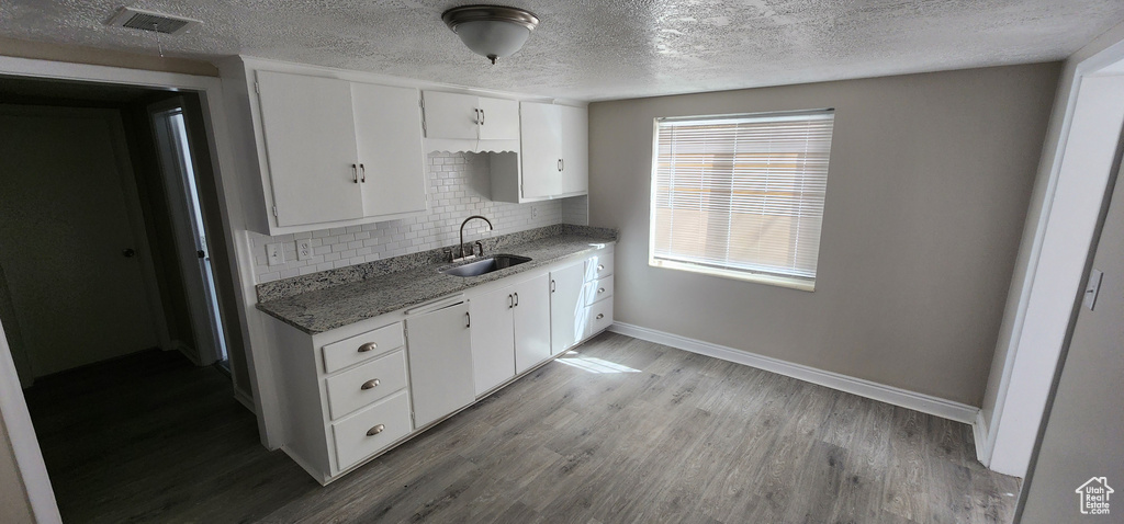 Kitchen featuring a sink, tasteful backsplash, baseboards, white cabinetry, and a textured ceiling