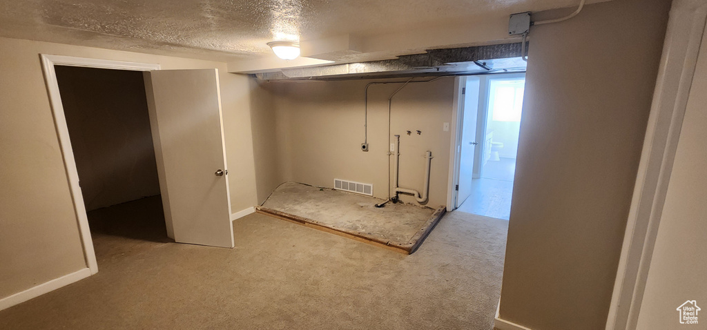 Basement featuring a textured ceiling, carpet, and baseboards