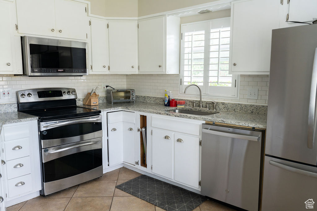 Kitchen with stainless steel appliances, a sink, backsplash, light tile patterned flooring, and white cabinetry