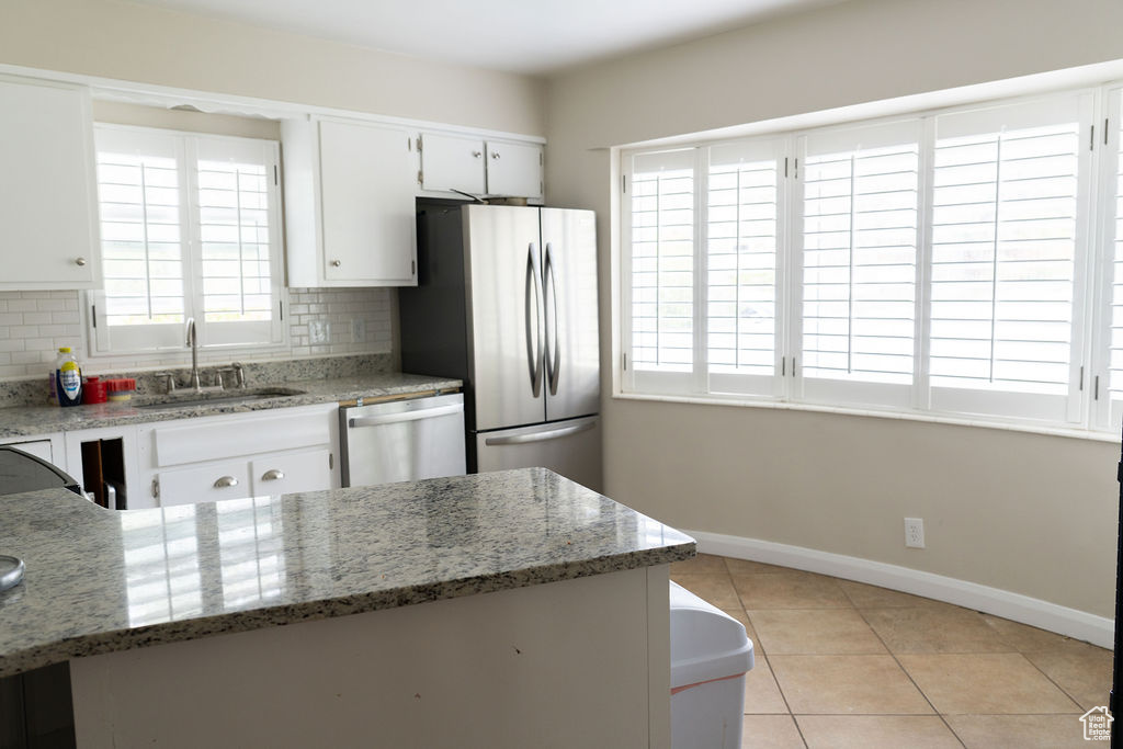 Kitchen featuring a sink, stainless steel appliances, decorative backsplash, baseboards, and light tile patterned flooring