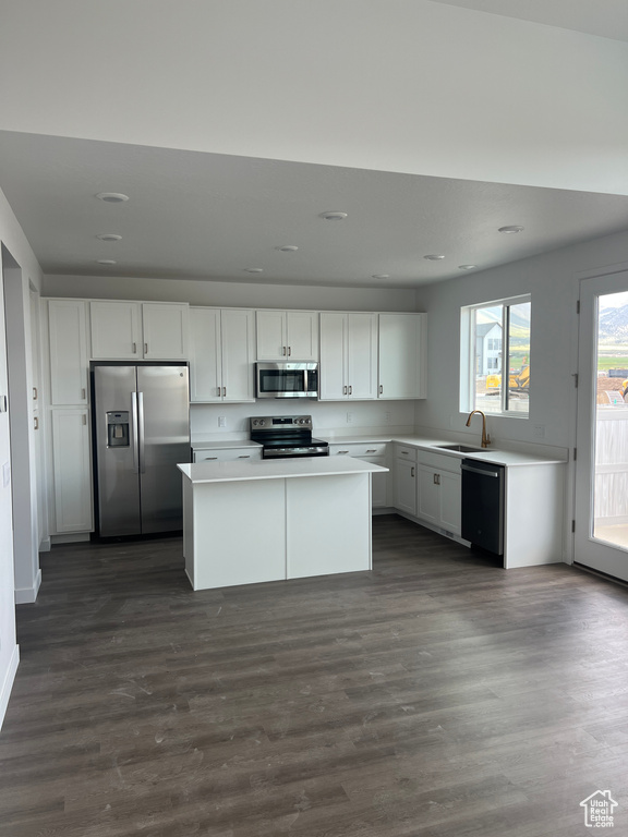 Kitchen with appliances with stainless steel finishes, a sink, light countertops, white cabinetry, and a center island
