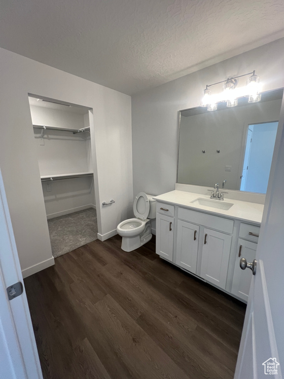 Bathroom featuring toilet, wood finished floors, vanity, a textured ceiling, and baseboards