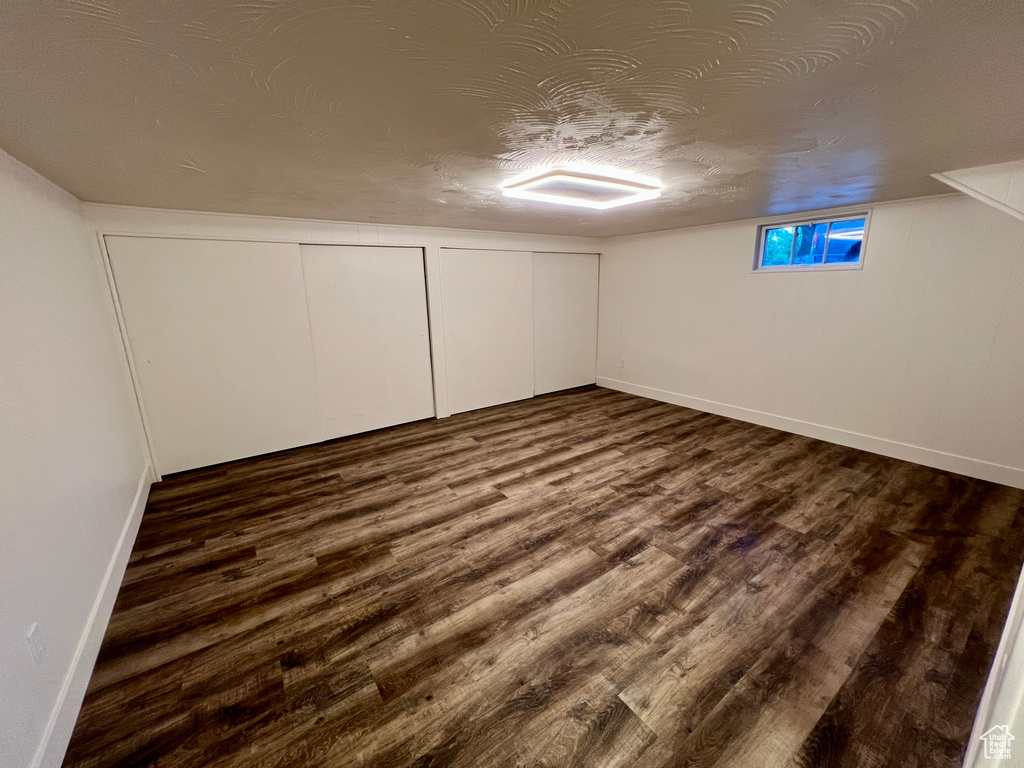 Basement with dark wood finished floors, baseboards, and a textured ceiling