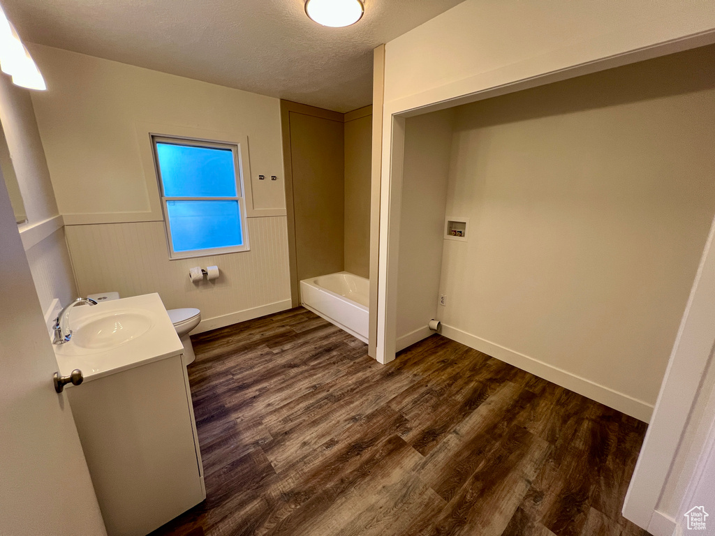 Bathroom with toilet, vanity, wood finished floors, a bath, and baseboards
