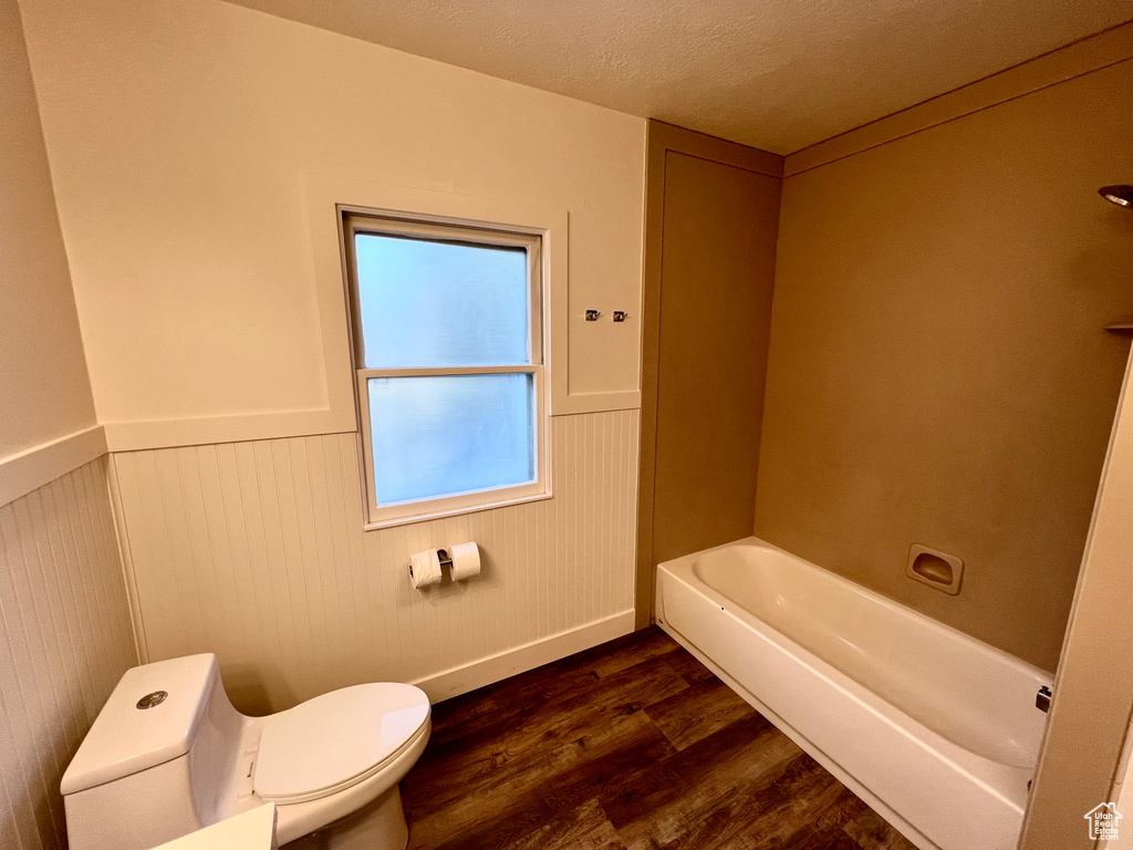 Full bath with toilet, wood finished floors, wainscoting, and a bathtub
