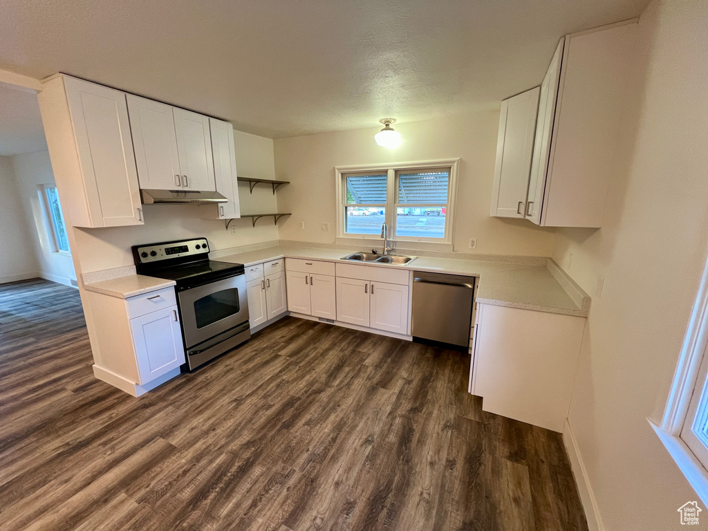 Kitchen with appliances with stainless steel finishes, a sink, dark wood-type flooring, and white cabinetry