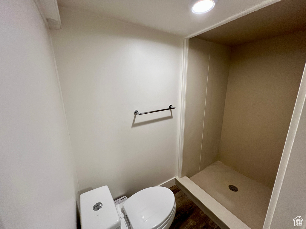 Bathroom featuring a shower stall, toilet, wood finished floors, and baseboards