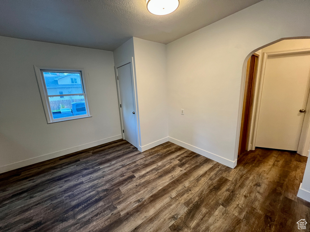 Unfurnished bedroom with dark wood-type flooring, arched walkways, baseboards, and a textured ceiling