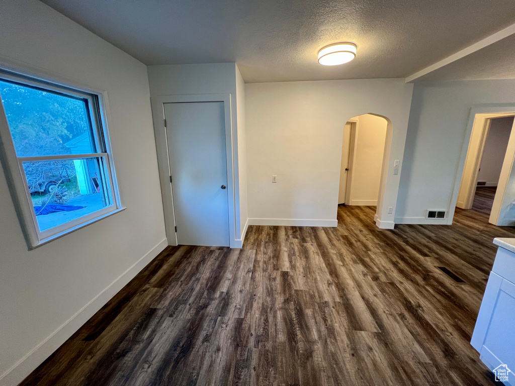 Unfurnished bedroom featuring arched walkways, dark wood finished floors, baseboards, and a textured ceiling