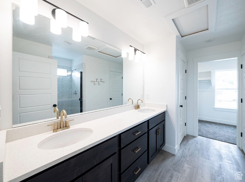 Bathroom featuring wood finished floors, double vanity, a stall shower, baseboards, and a walk in closet