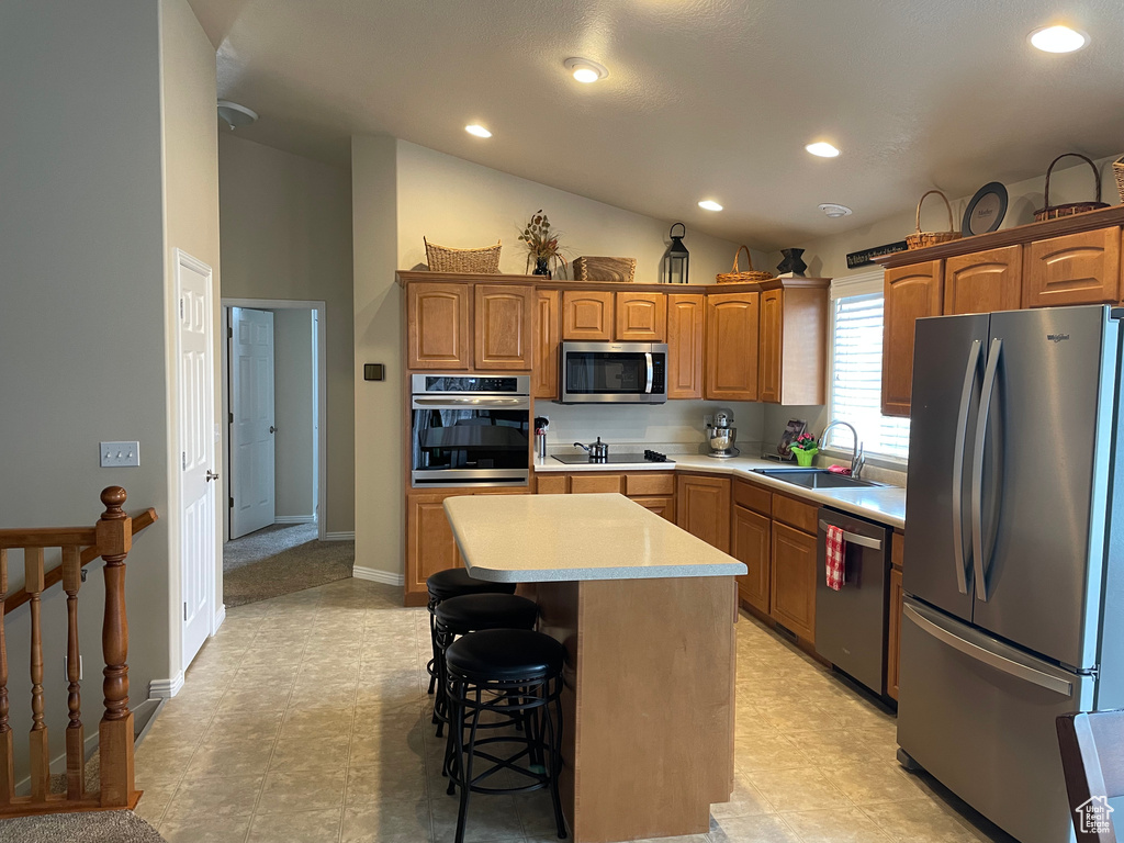 Kitchen featuring a sink, light countertops, appliances with stainless steel finishes, a center island, and brown cabinetry