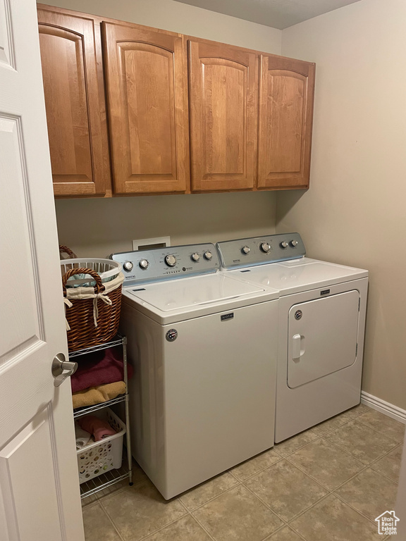 Laundry room featuring cabinet space, light tile patterned floors, baseboards, and independent washer and dryer
