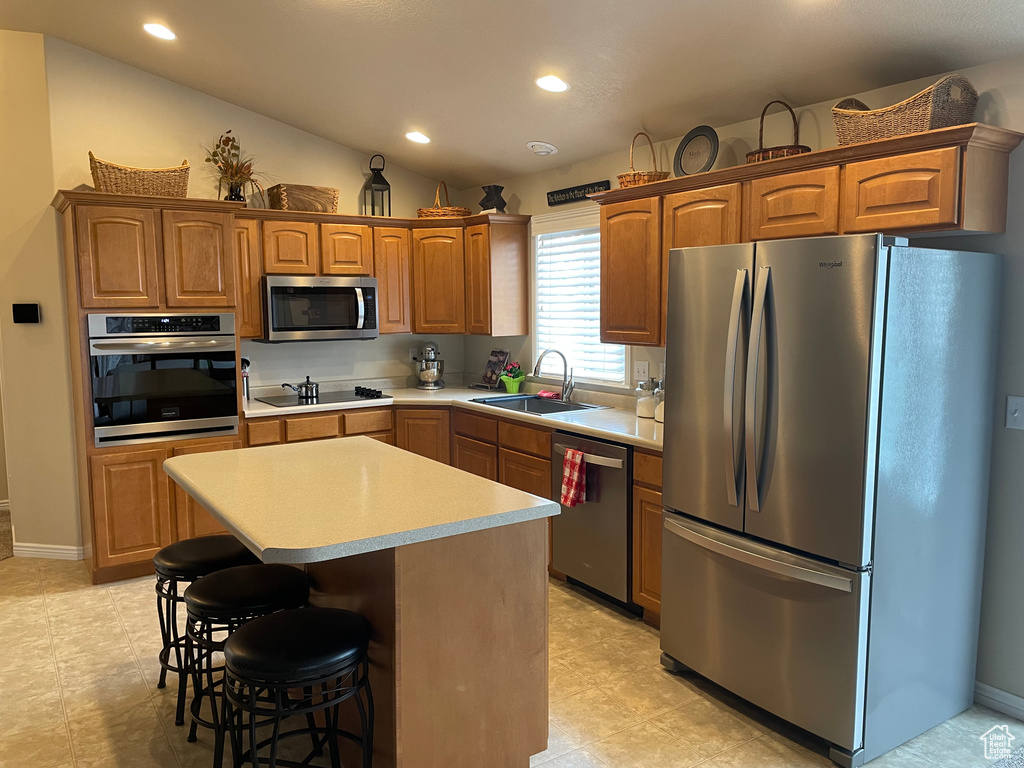 Kitchen featuring stainless steel appliances, a sink, a kitchen island, light countertops, and brown cabinets