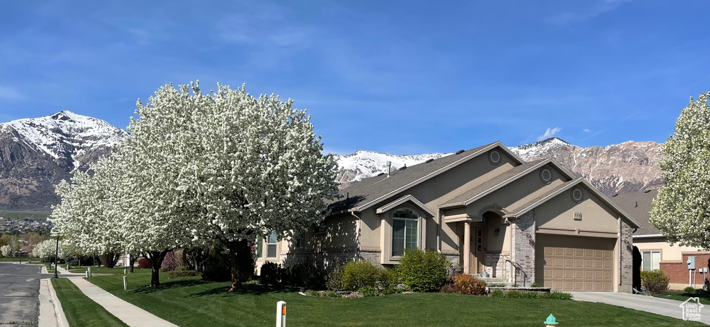 View of front of home with a garage, driveway, a front lawn, and a mountain view