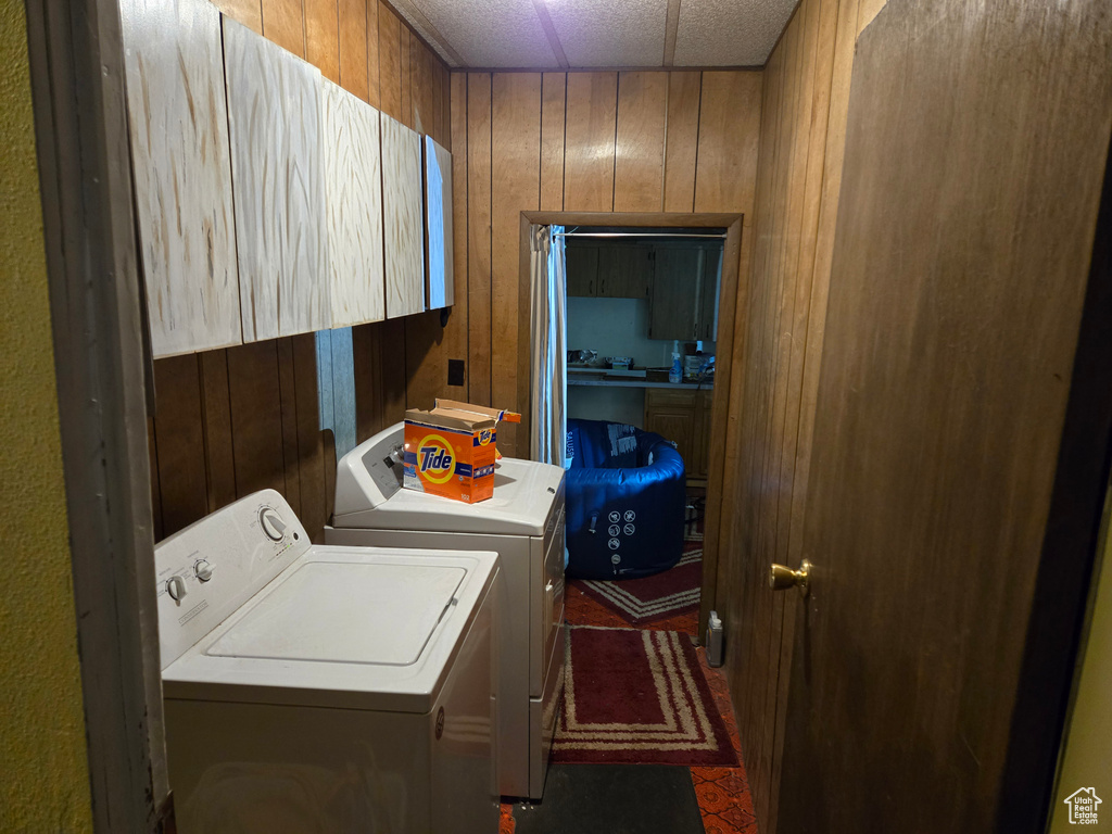 Washroom featuring washer and clothes dryer, wood walls, and cabinet space