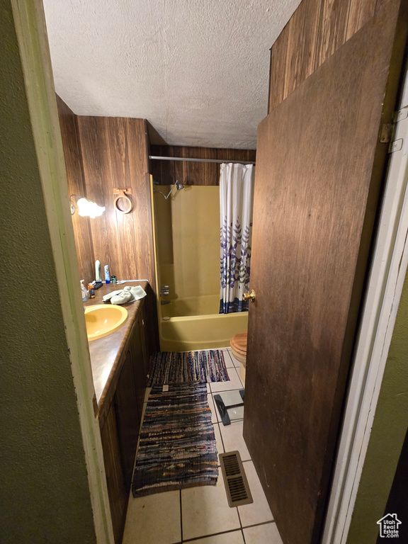 Full bath with tile patterned floors, a textured ceiling, shower / bath combo, double vanity, and toilet