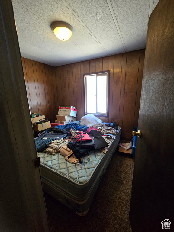Bedroom featuring wooden walls, carpet, and a textured ceiling