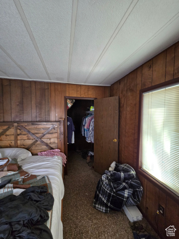 Bedroom with wooden walls, carpet flooring, a spacious closet, a textured ceiling, and a closet