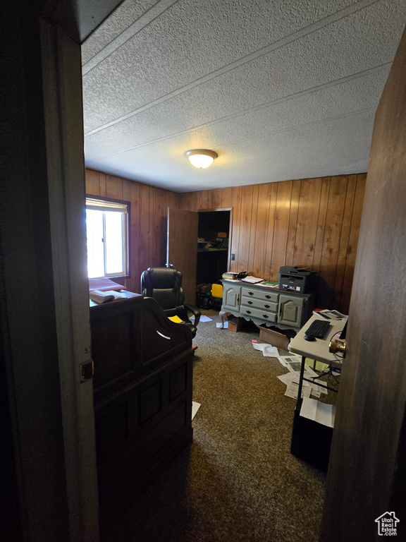 Bedroom with a desk, wood walls, carpet floors, and a textured ceiling