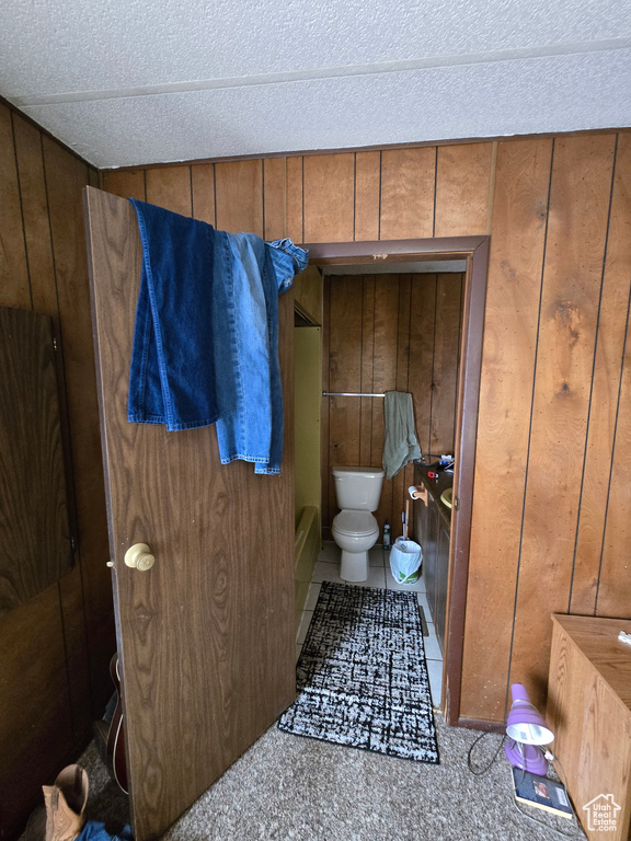 Bathroom with wood walls, toilet, a tub to relax in, and a textured ceiling