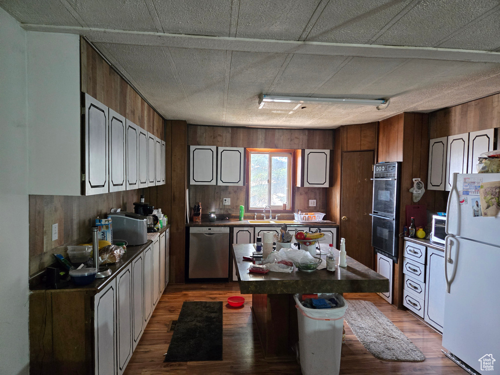 Kitchen with freestanding refrigerator, dishwasher, wood walls, a sink, and wood finished floors
