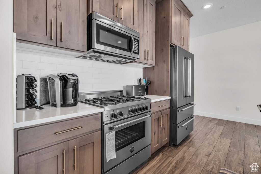 Kitchen with high quality appliances, tasteful backsplash, dark wood-style floors, light countertops, and recessed lighting