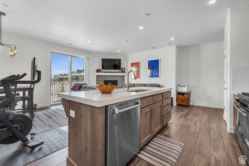 Kitchen with a sink, stainless steel dishwasher, light countertops, wood finished floors, and recessed lighting