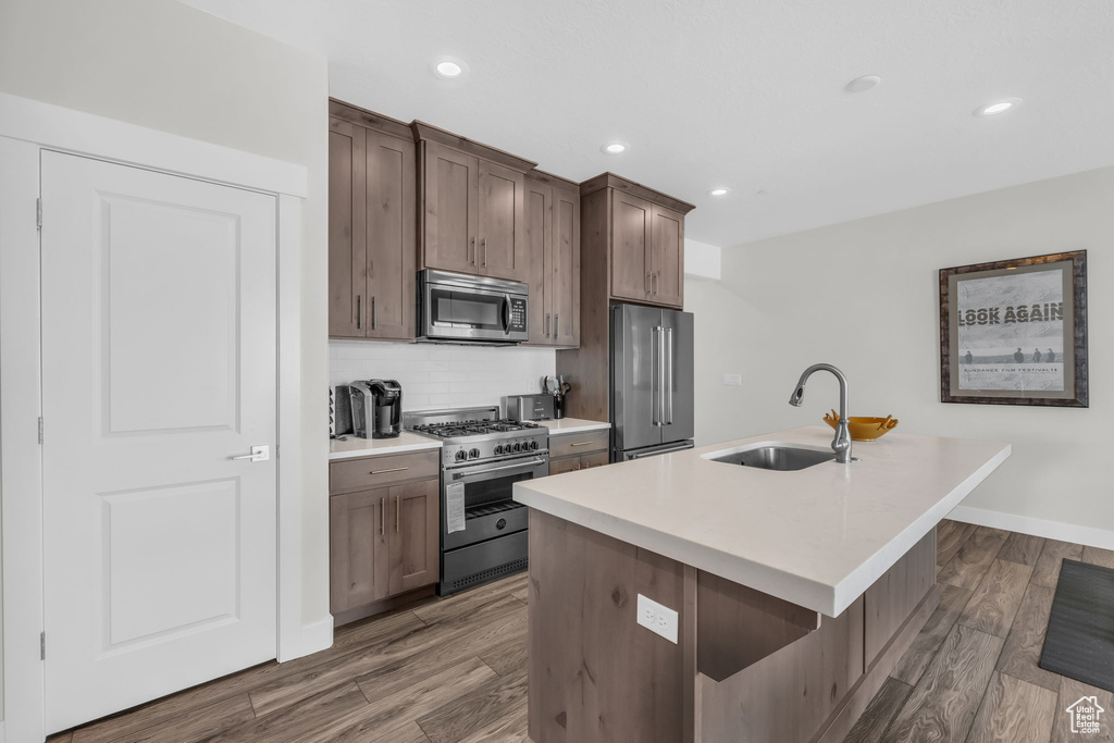 Kitchen featuring high quality appliances, a sink, an island with sink, dark wood-type flooring, and backsplash