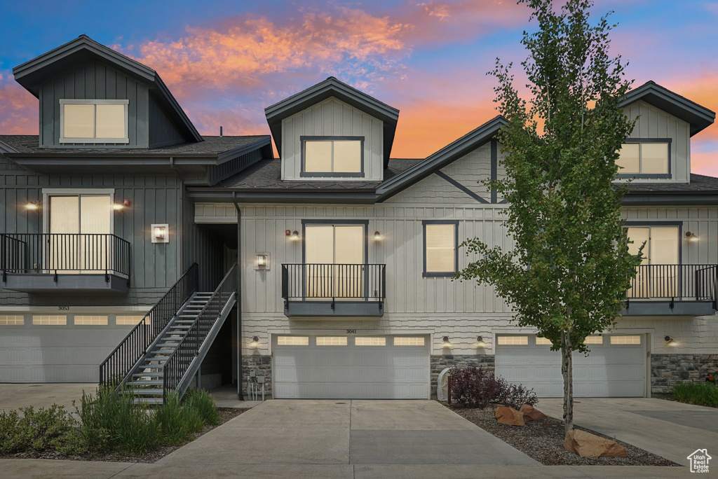Townhome / multi-family property featuring roof with shingles, an attached garage, stone siding, concrete driveway, and stairs