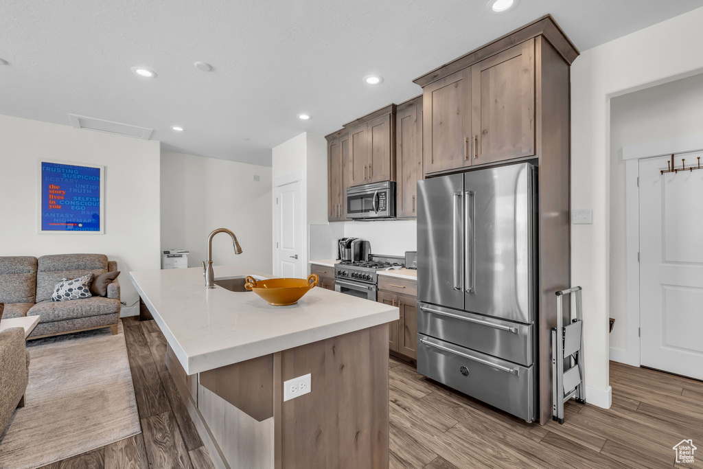 Kitchen with high end appliances, a sink, a center island with sink, open floor plan, and wood finished floors