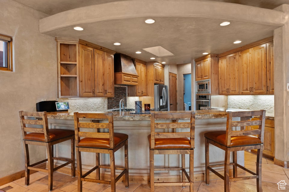 Kitchen with premium range hood, appliances with stainless steel finishes, a peninsula, recessed lighting, and open shelves