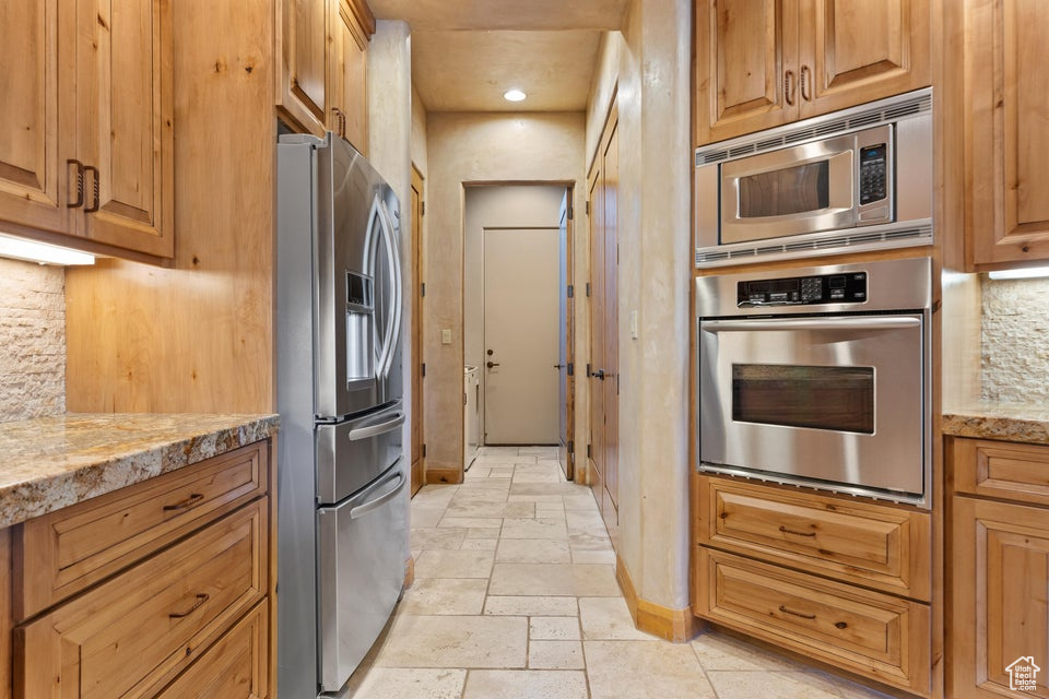 Kitchen with appliances with stainless steel finishes, baseboards, stone tile flooring, tasteful backsplash, and light stone countertops