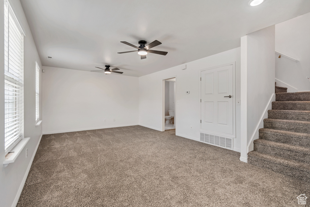 Carpeted empty room with ceiling fan, stairway, and baseboards