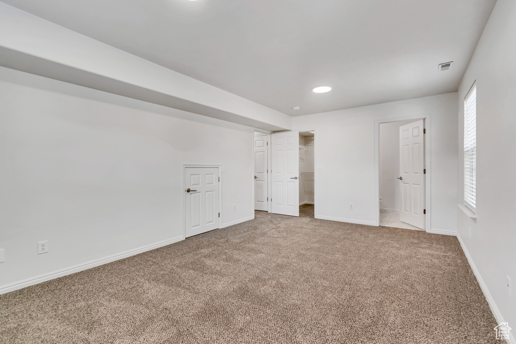 Unfurnished bedroom featuring carpet, baseboards, recessed lighting, and a walk in closet