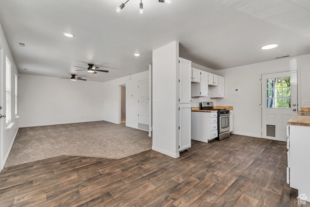 Kitchen featuring stainless steel gas stove, dark wood-style flooring, a ceiling fan, white cabinetry, and baseboards